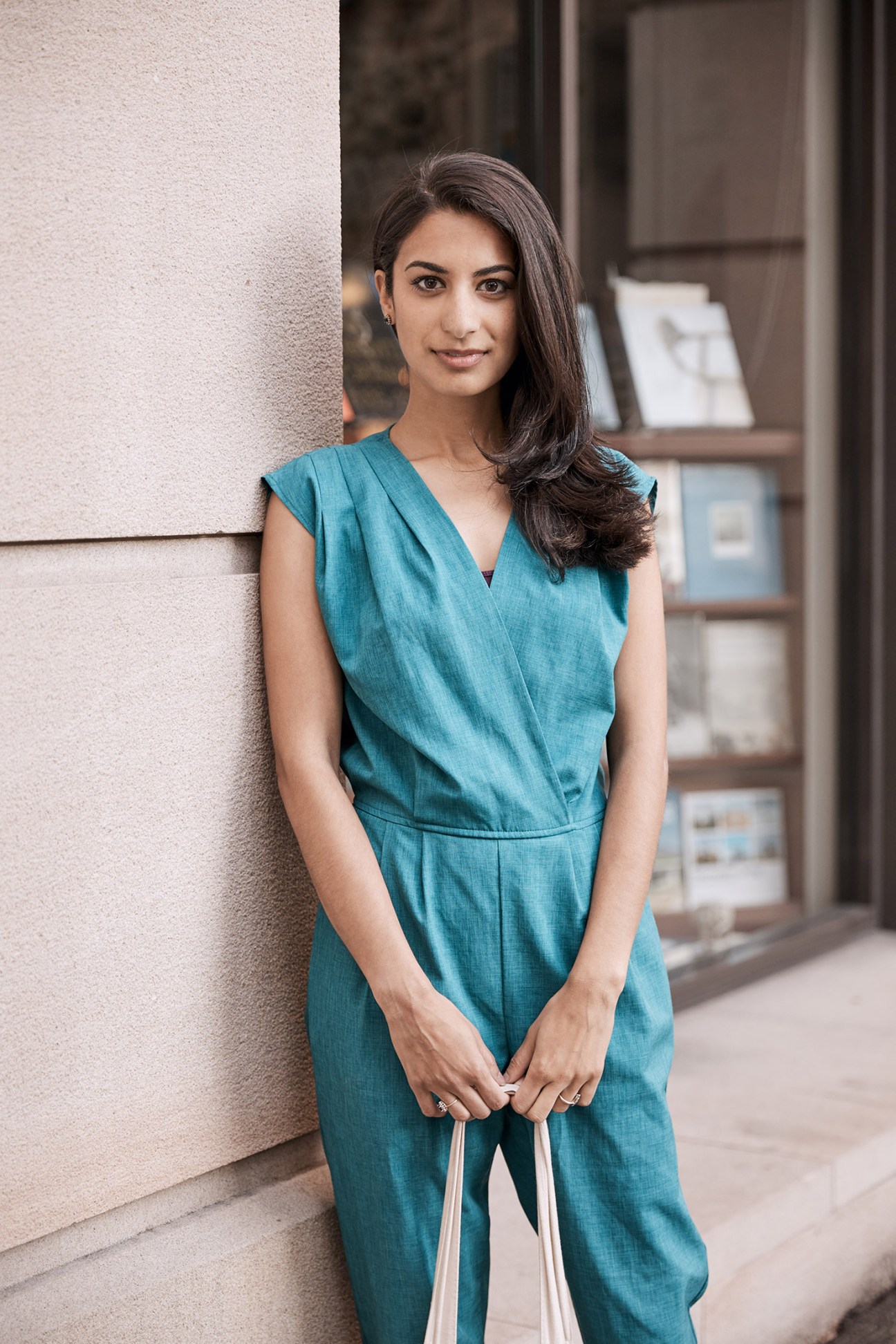 Woman in teal wrap dress standing against textured wall in urban setting