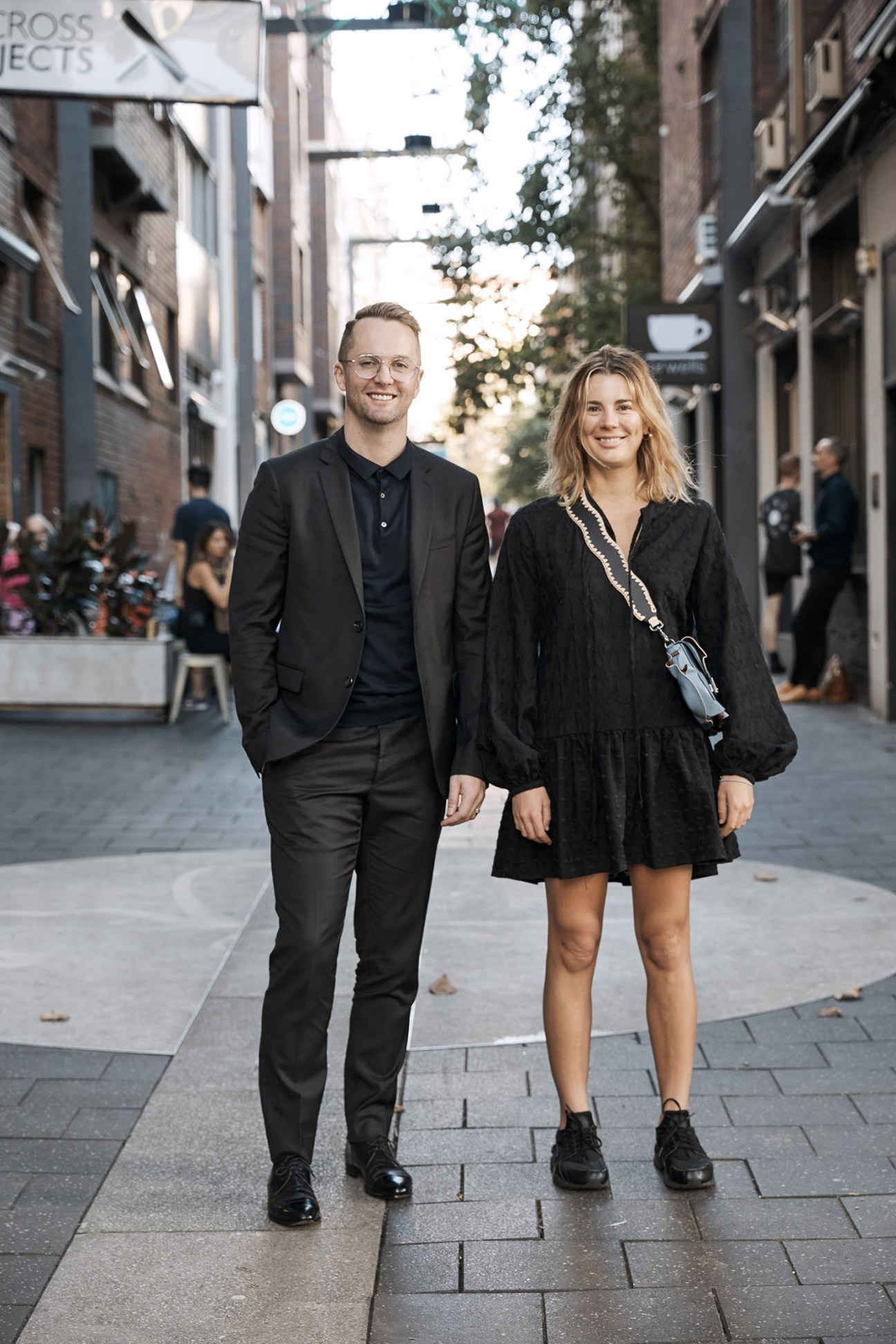 Two people smiling while walking down a street in an urban shopping district.