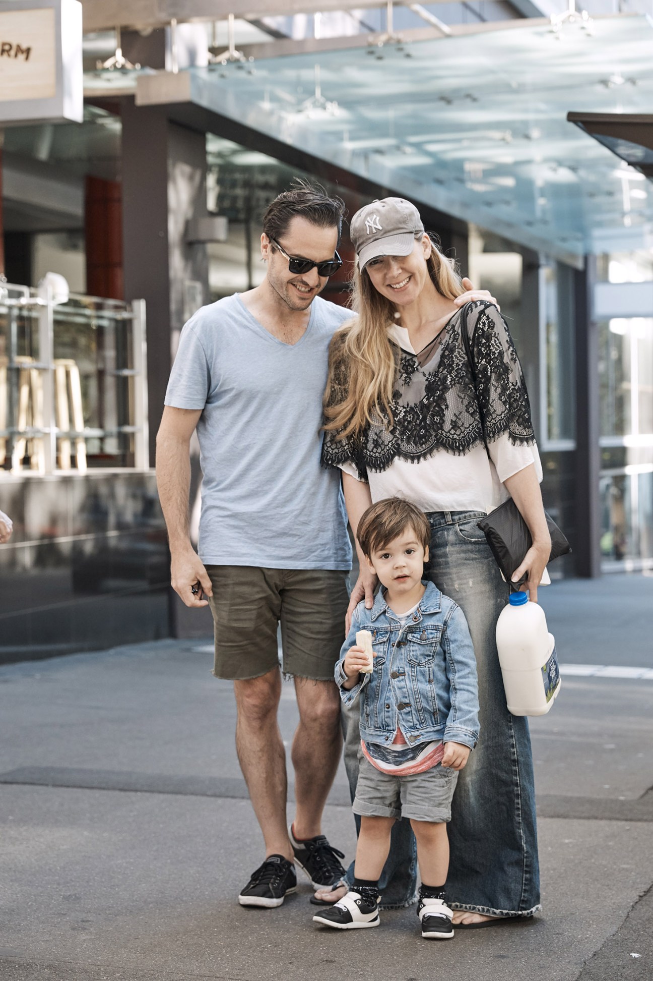A man, woman and young child stand together on a city street smiling at the camera.