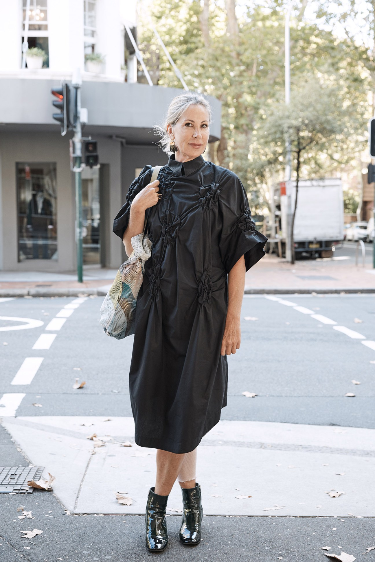 Woman with white hair wearing a black textured shirt and mesh shoulder bag on a Sydney street.