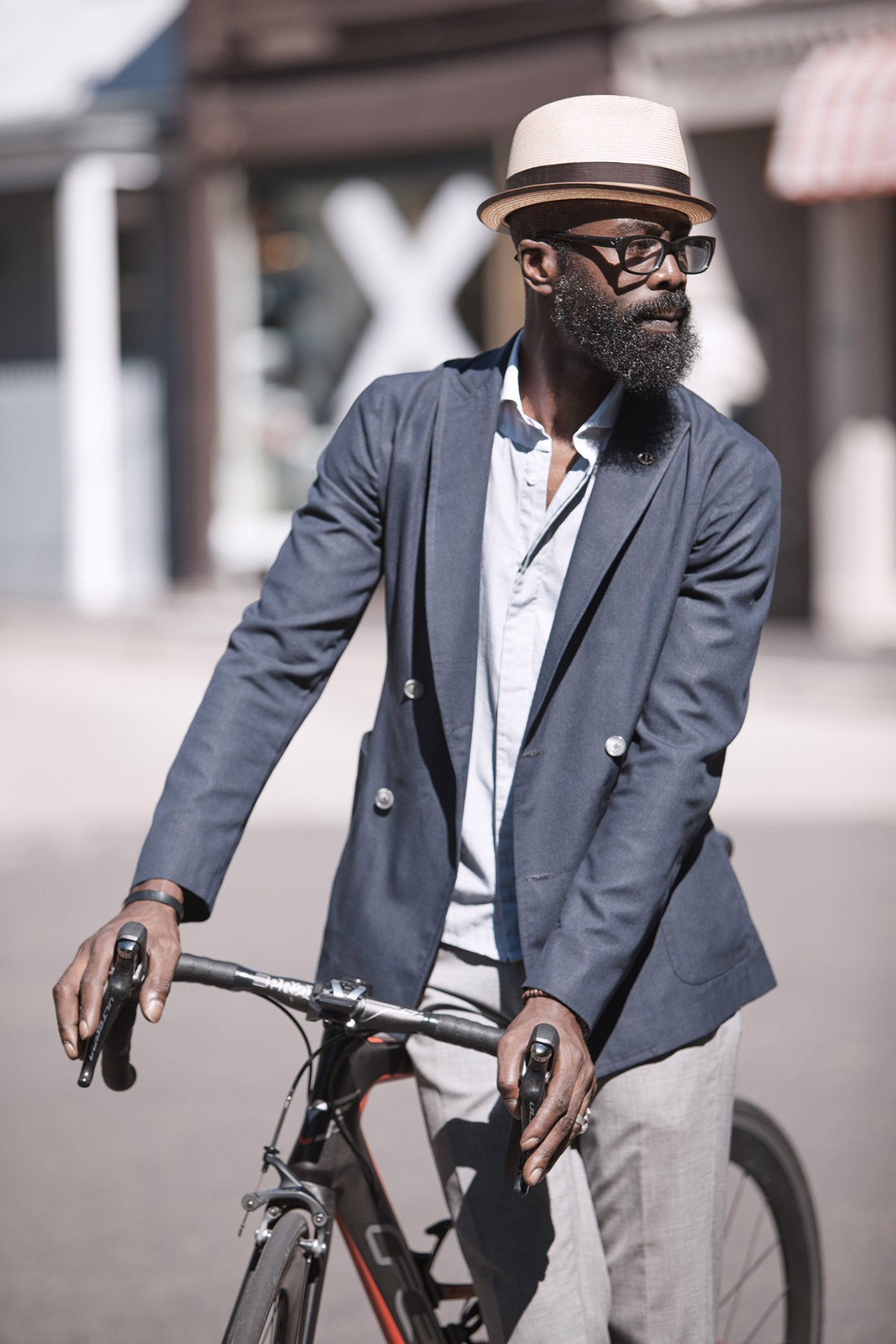 Man in blue blazer and white panama hat riding a bicycle on city street
