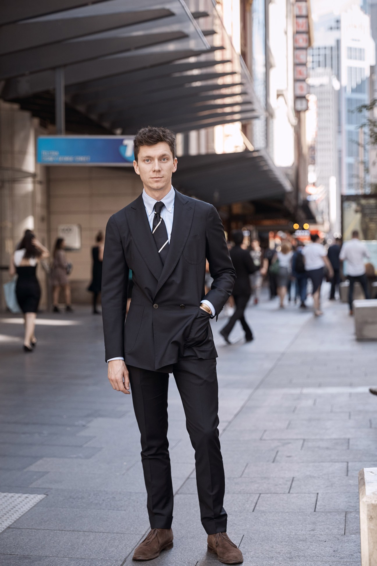 Man in dark double-breasted blazer and striped tie standing on city street.