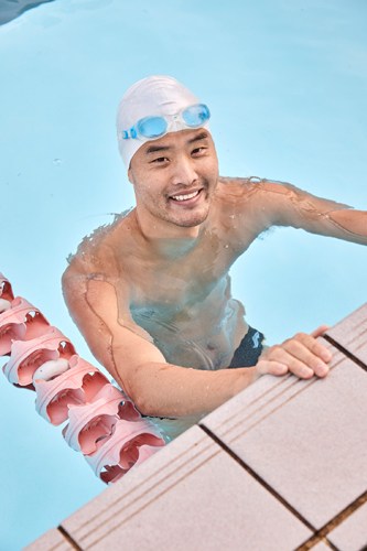 A swimmer in goggles and white swim cap smiles at the edge of North Sydney Olympic Pool.