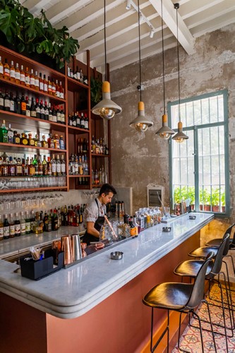 A bartender serves drinks at a counter in a room with exposed concrete walls and wooden shelving.