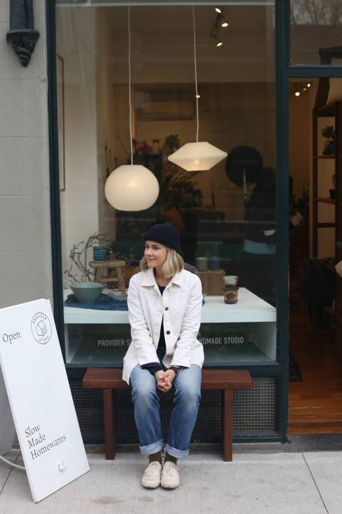 Woman sitting on a bench outside Provider Store in Sydney, with pendant lights visible through the window behind her.