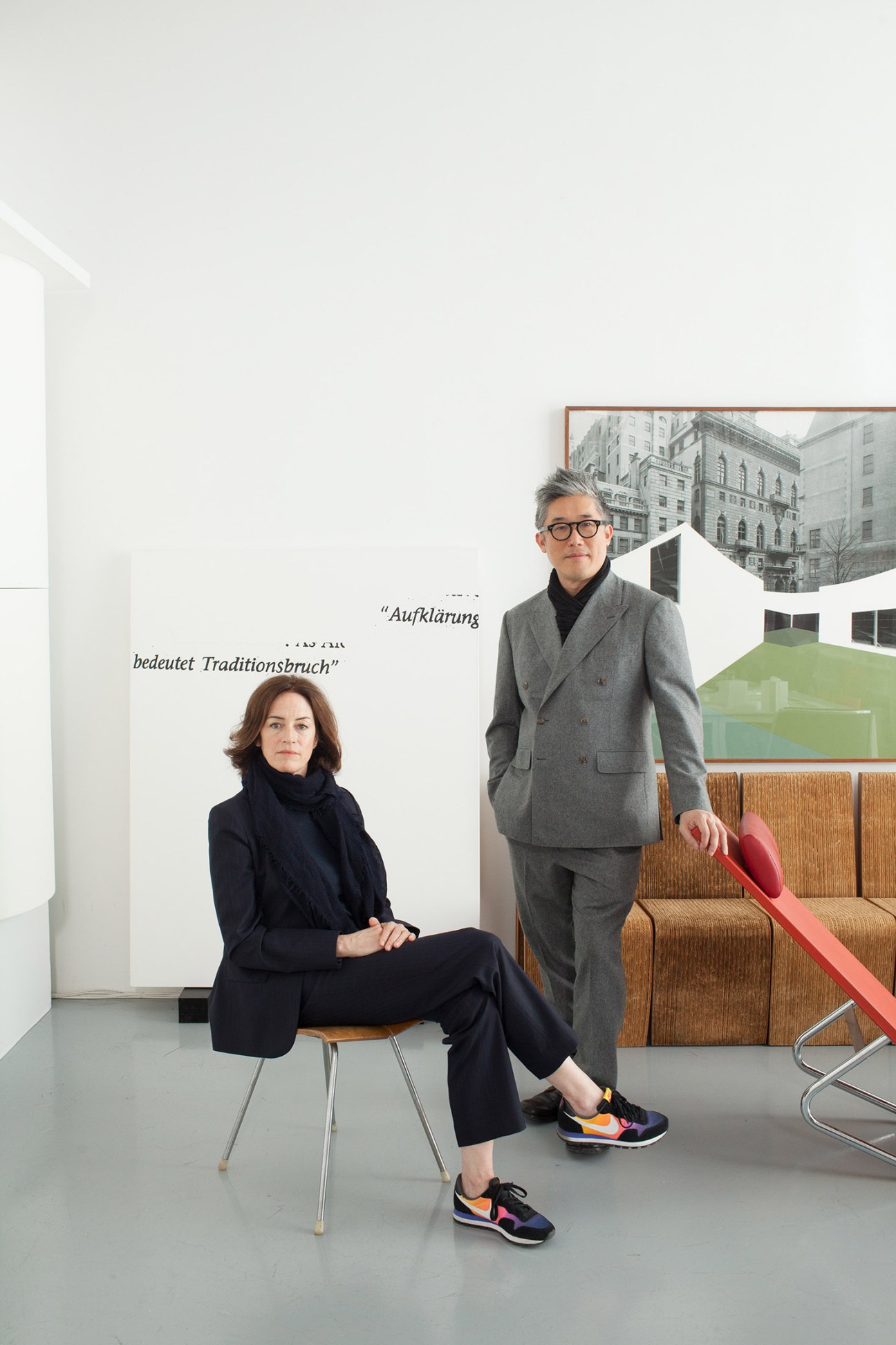 Two people posing in a modern retail space with architectural elements and urban backdrop visible through windows.