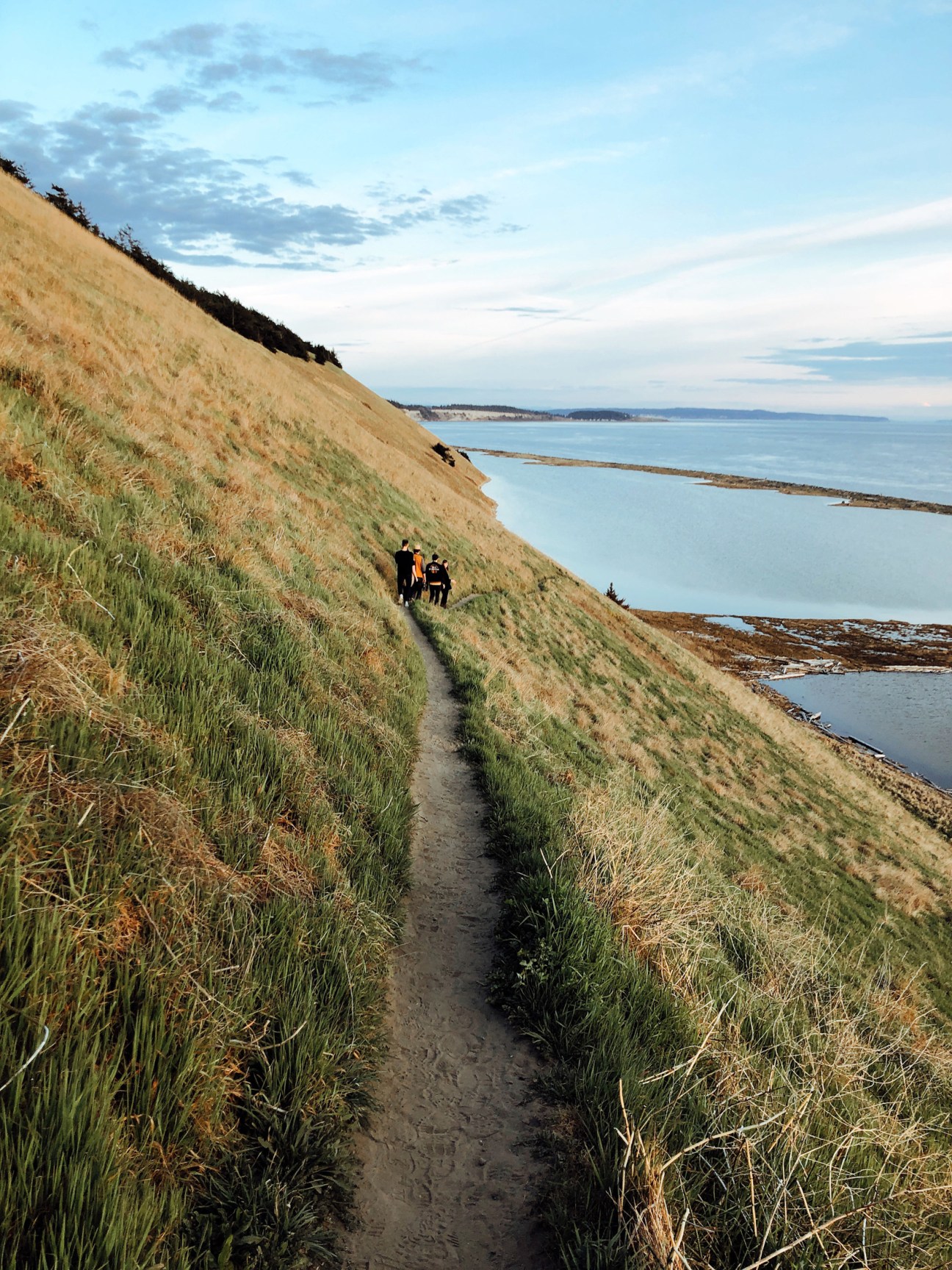 Hikers walking along a coastal cliff path overlooking calm blue waters and distant shoreline