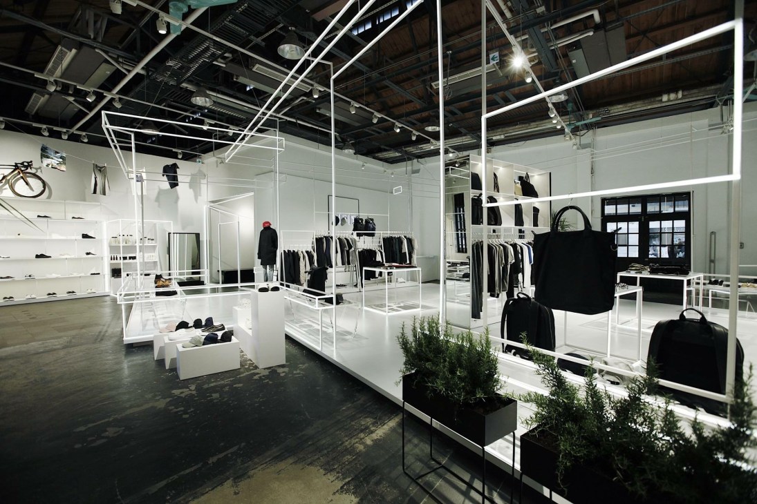 Interior of DPT multibrand shop in Taipei featuring minimalist white display cases with clothing and accessories against industrial ceiling.