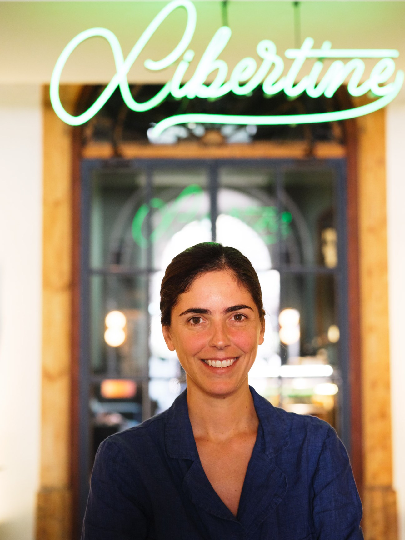 Inés Miro Sans, co-owner of Casa Bonay hotel, smiling in front of the hotel's neon sign in Barcelona.