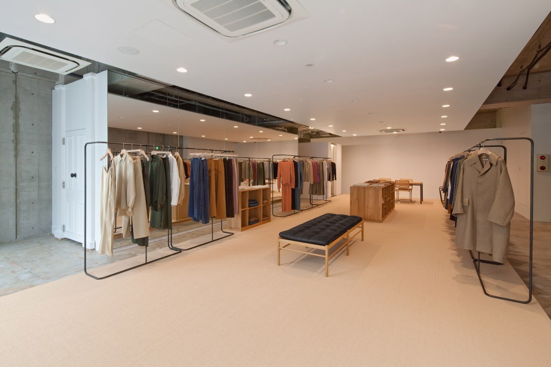 Auralee flagship store interior in Tokyo's Aoyama neighbourhood with clothing on minimal iron racks and mid-century furniture.