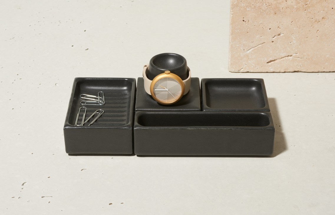 Black 3D-printed porcelain organizer with compartments holding paper clips and a watch with wooden bezel.