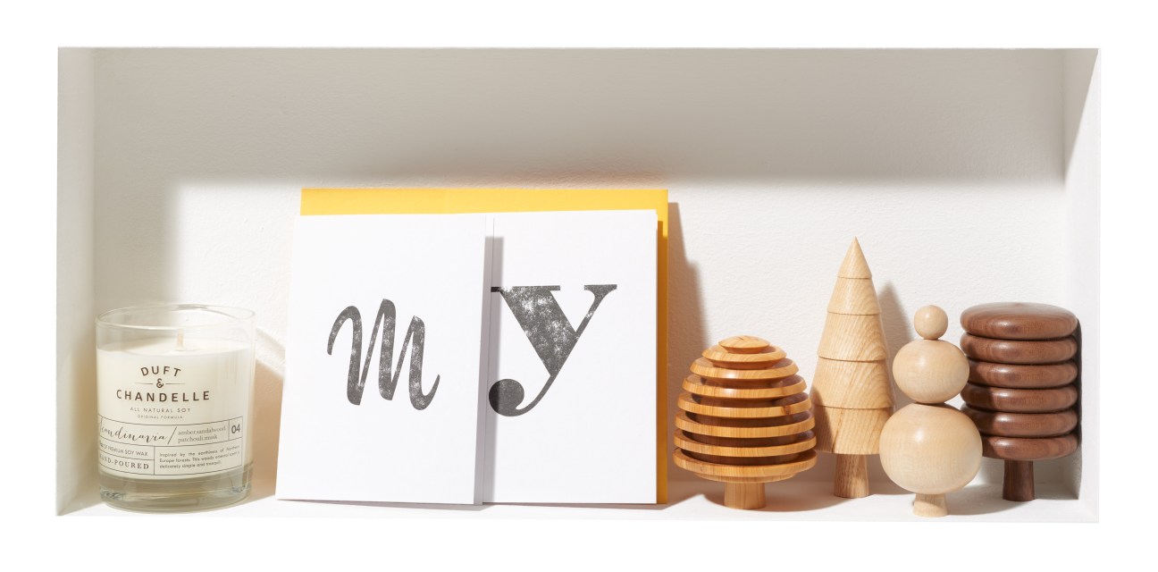 Styled arrangement featuring a scented candle, letterpress card with yellow frame, and wooden decorative objects.