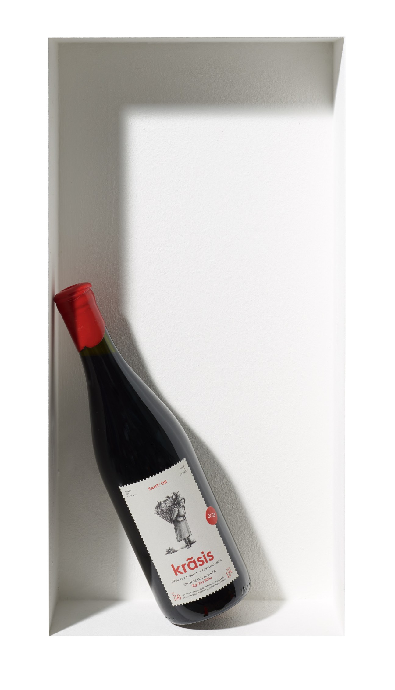 Krasis red wine bottle with red foil cap and white label against white wall.