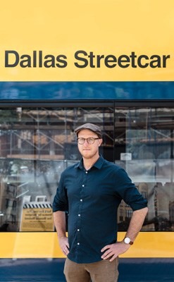 Jason Roberts standing in front of a yellow and blue Dallas Streetcar.