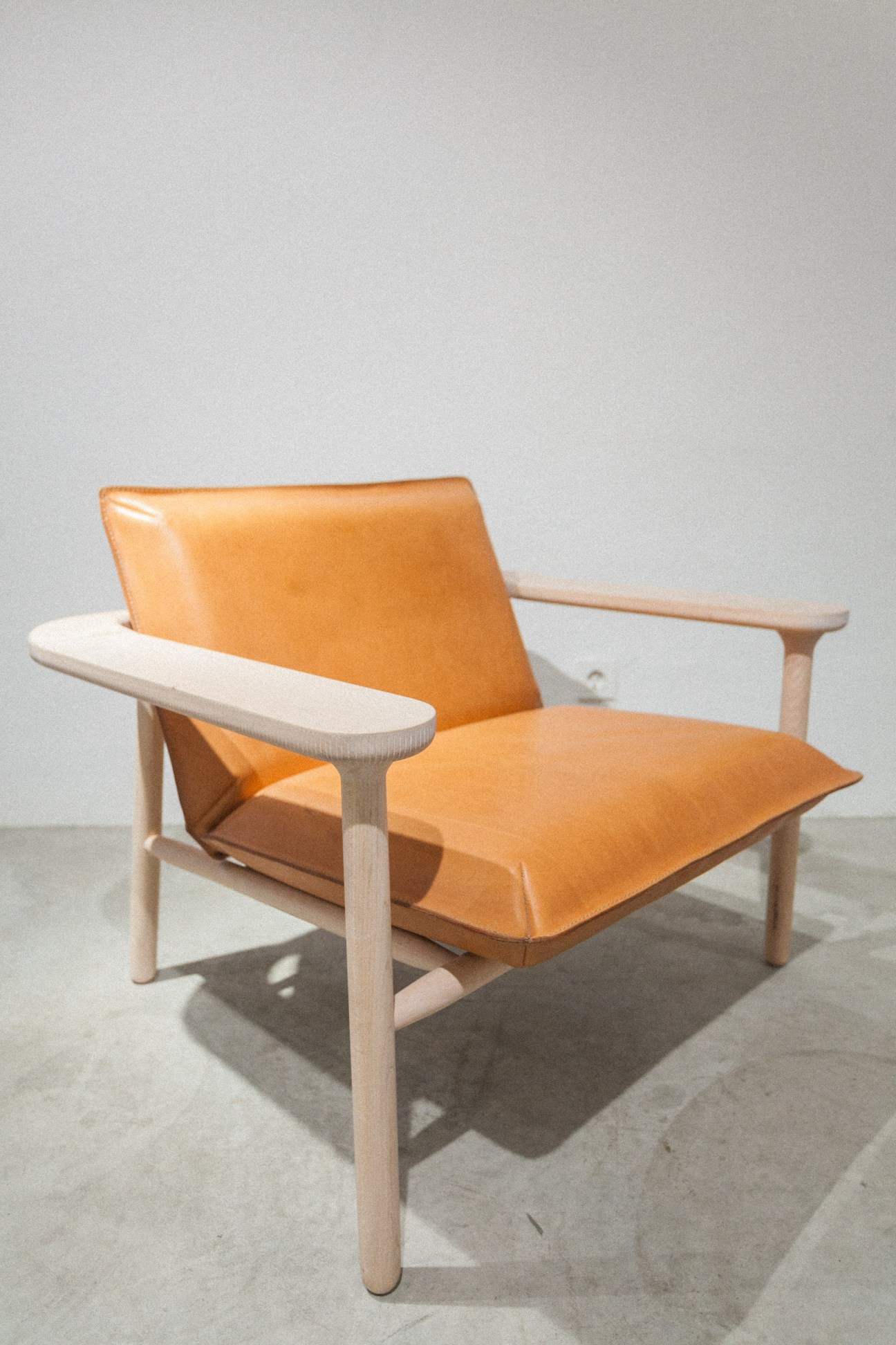Natural wood armchair with tan leather seat and back, cylindrical wooden frame and arms.