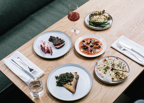 Overhead view of plated dishes at Erst restaurant including toast with greens, pizza, and seafood appetizers.