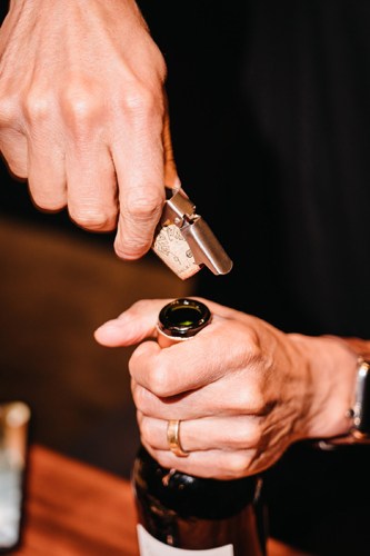 Close-up of hands holding a wine bottle and glass against a dark background.