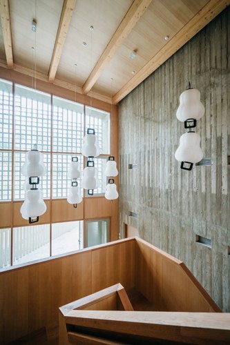 Interior of Swiss embassy in Seoul featuring white pendant lights, wooden ceiling beams, and concrete walls.