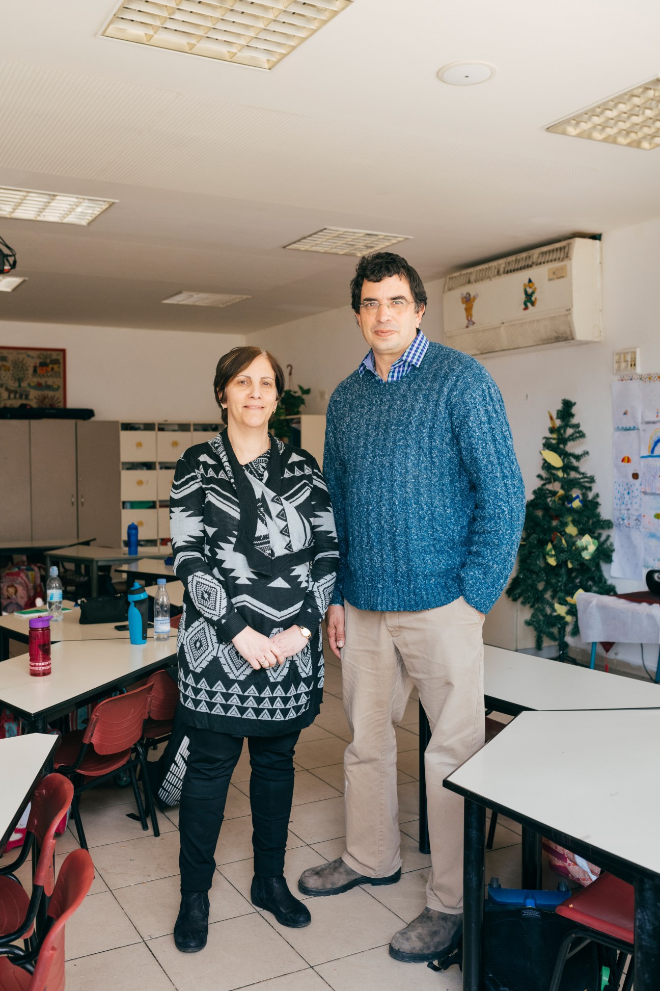 Nadia Kinani and Arik Saporta stand together in a Hand in Hand school classroom decorated with children's artwork.