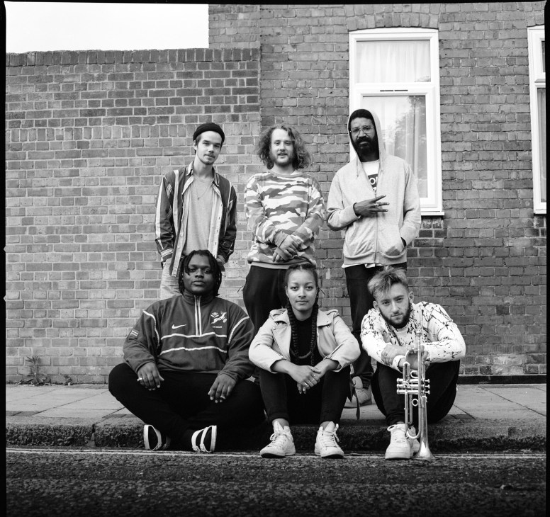 Black and white portrait of six young London jazz musicians posing against a brick wall