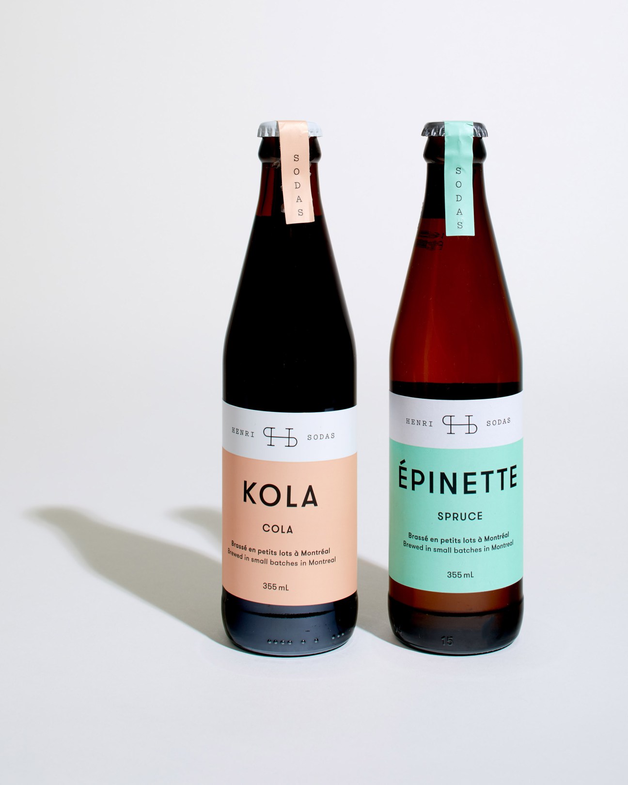Two Henri Sodas bottles: a cola with peach-colored label and a spruce beer with mint-green label.