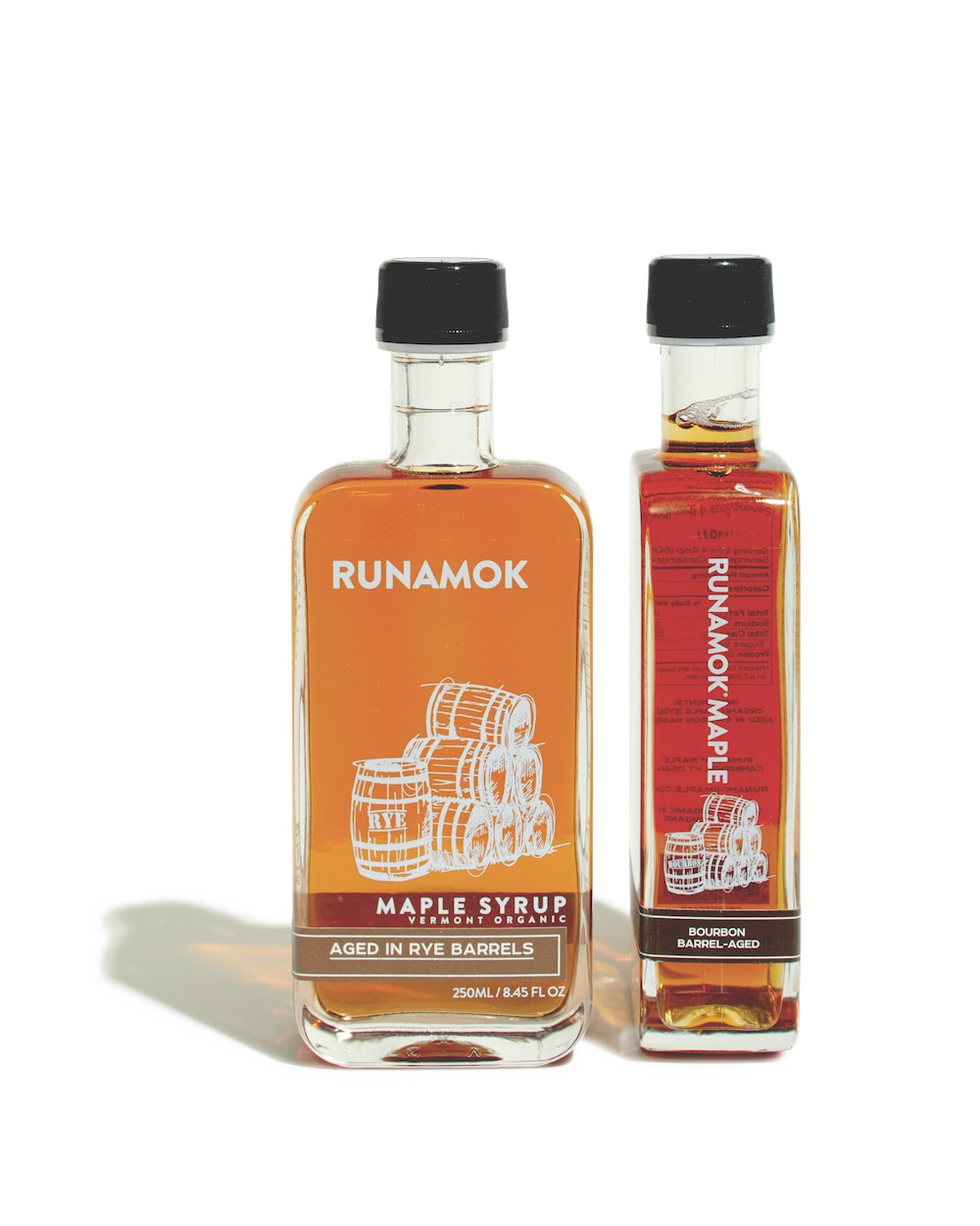 Two Runamok maple syrup bottles with black caps, one aged in rye barrels and one barrel-aged bourbon.