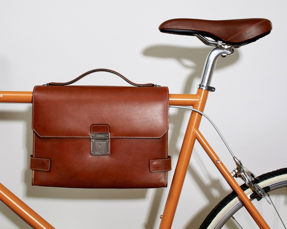 Brown leather briefcase attached to an orange bicycle frame with brown saddle.