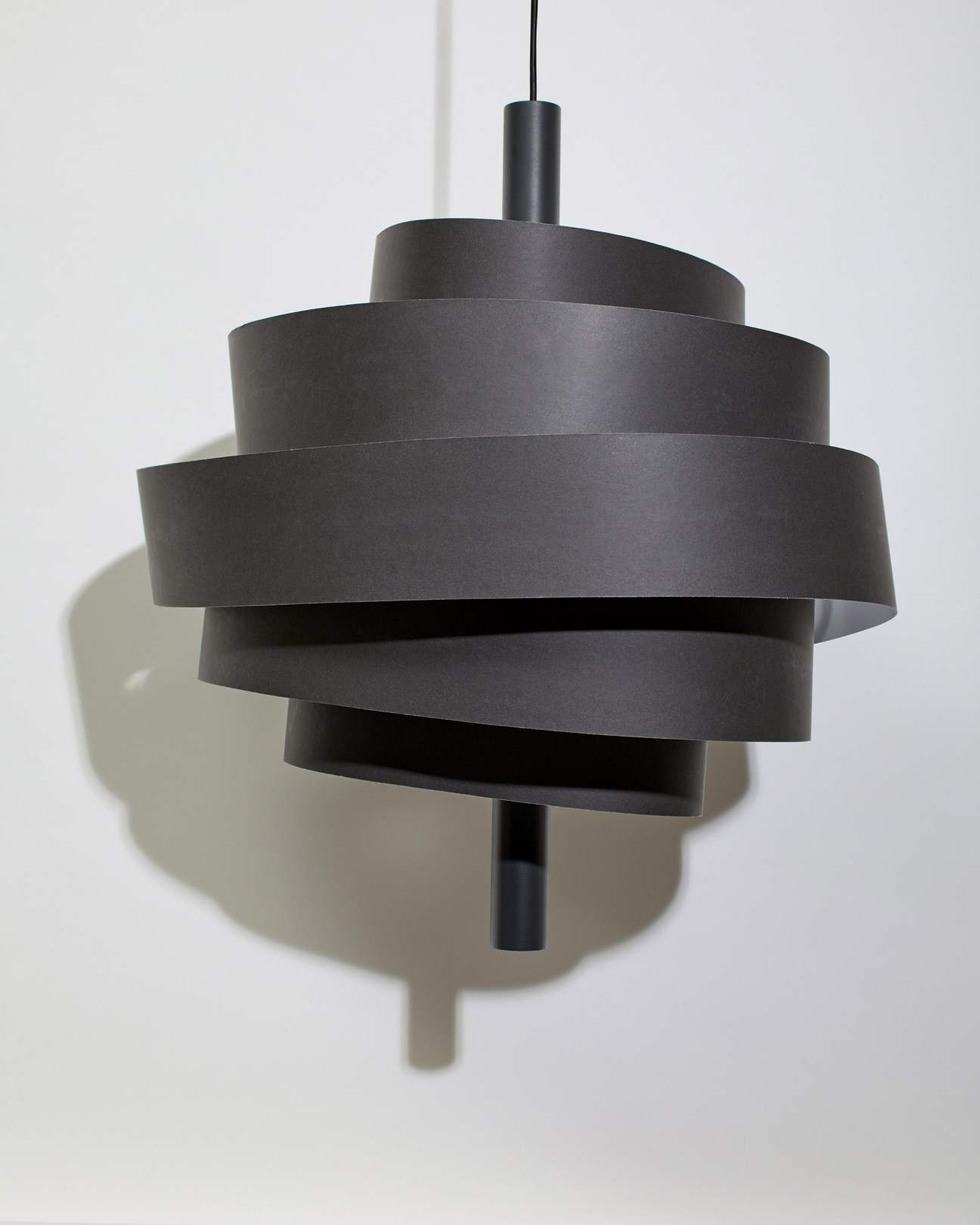 Marset Piola lamp with spiralling laminated bands in graphite finish hanging from black cord.