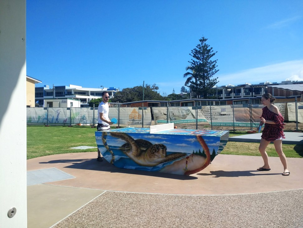 Two people playing table tennis outdoors at a public table in Kingscliff, Australia.