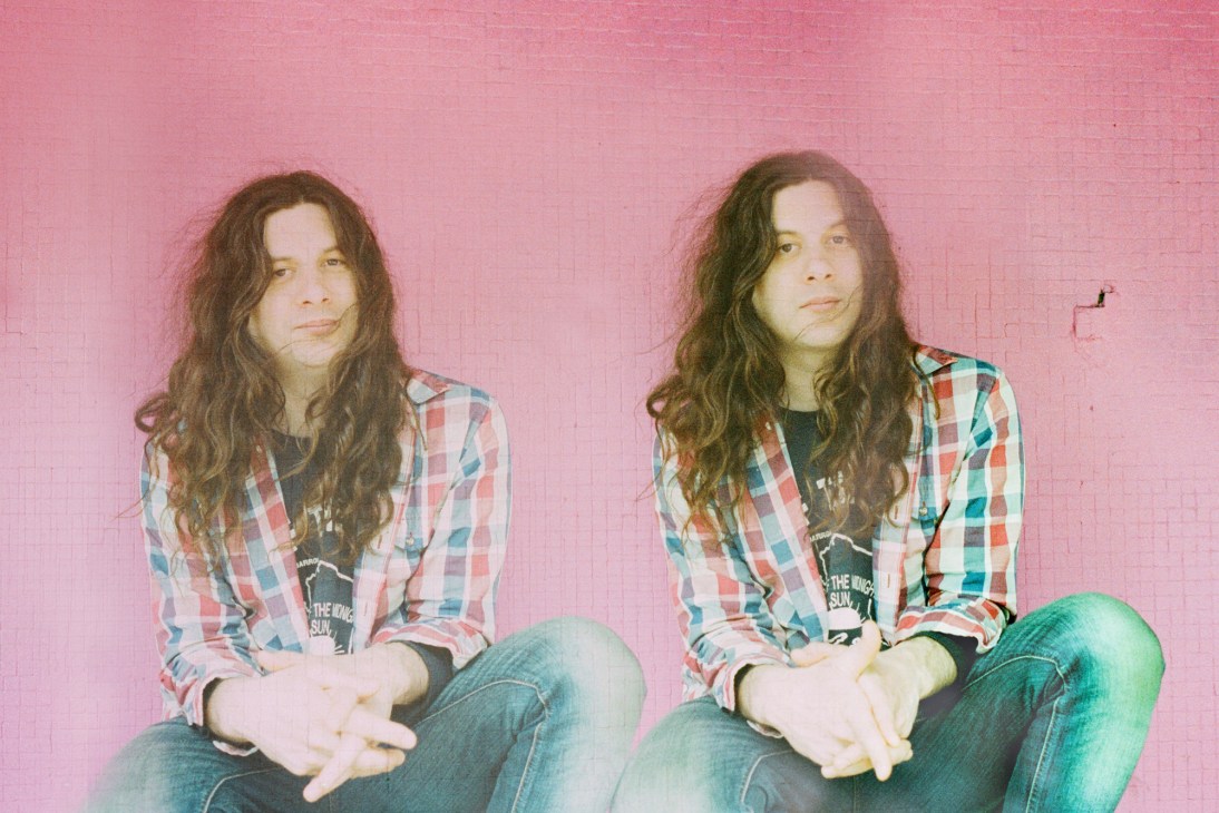 Portrait of Kurt Vile, musician, against a pink background.