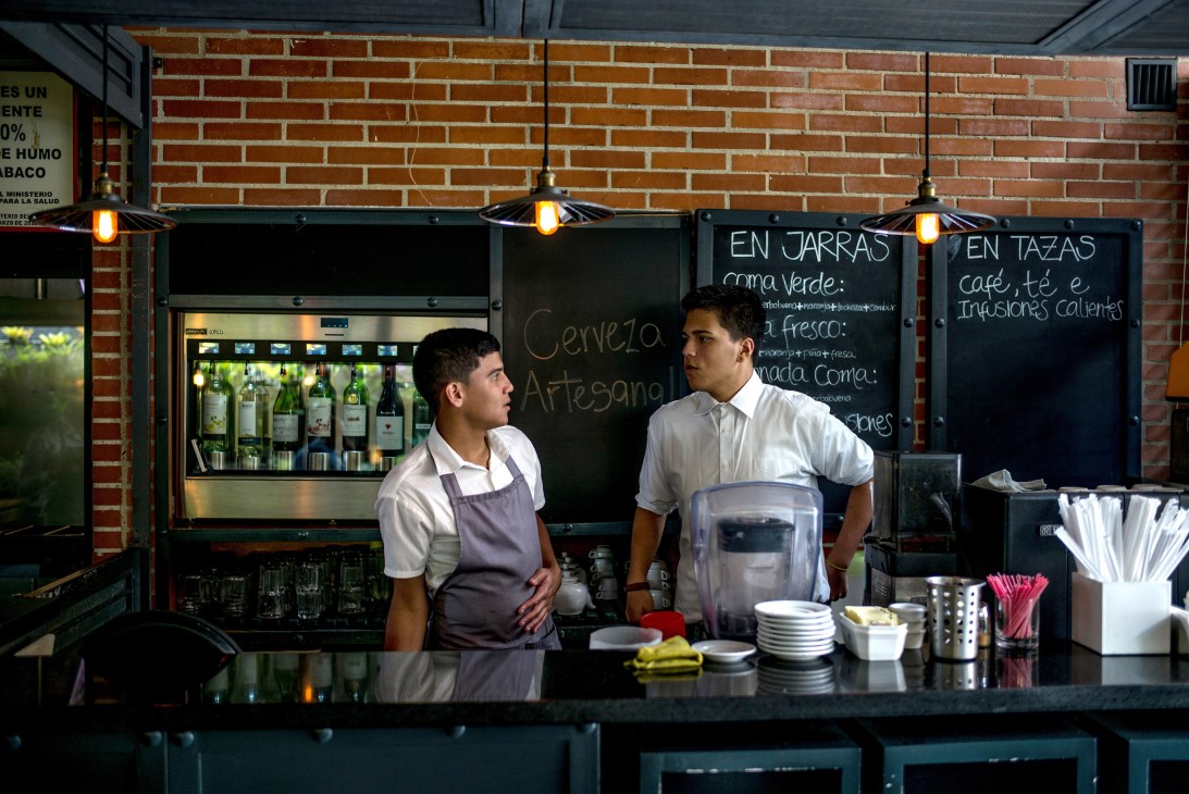 Two men in white shirts working behind a bar counter with bottles displayed on shelves