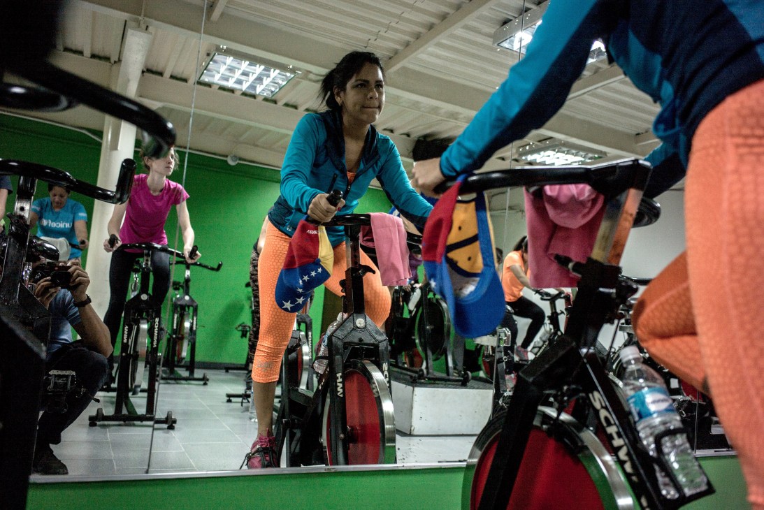 A woman in colorful workout clothes rides a stationary bike in a fitness class