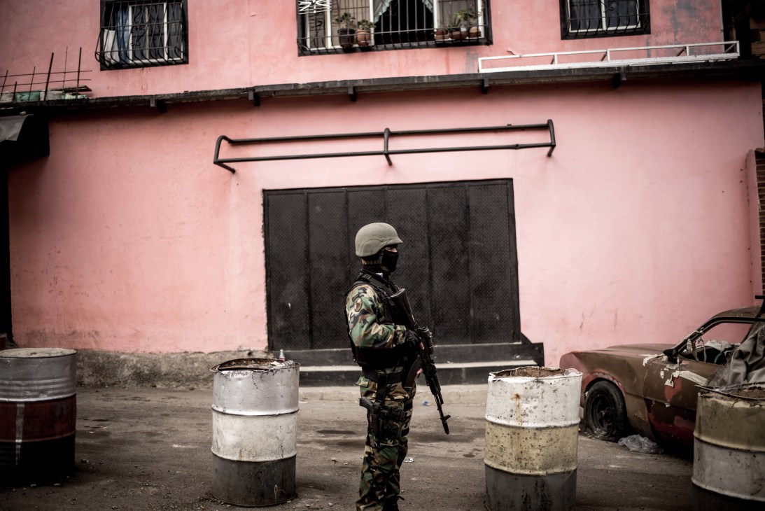 Armed soldier in camouflage uniform and helmet standing guard on a street with concrete barriers and pink building