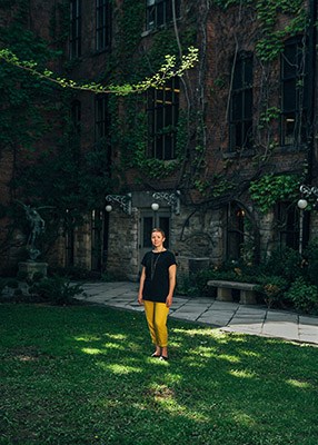 Michelle Senayah stands in a laneway with green space, ivy-covered walls and paved ground in Toronto.