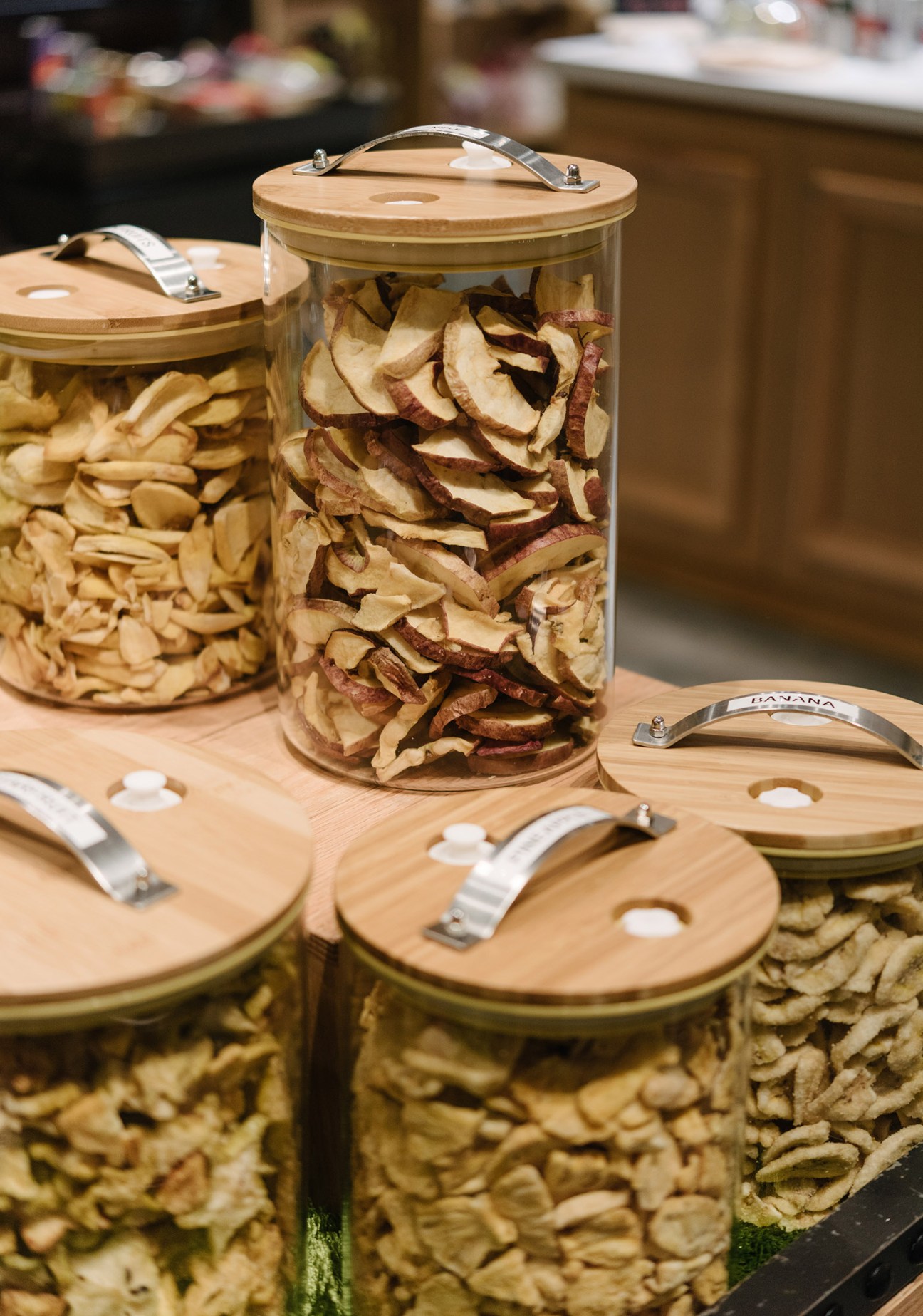 Glass containers filled with unpackaged dried foods including pasta, cereal, and coconut slices from various origins.