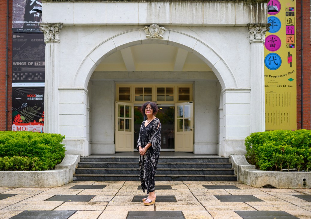 Yuki Pan, director of Museum of Contemporary Art Taipei, stands in front of the museum's classical neoclassical entrance with white columns.