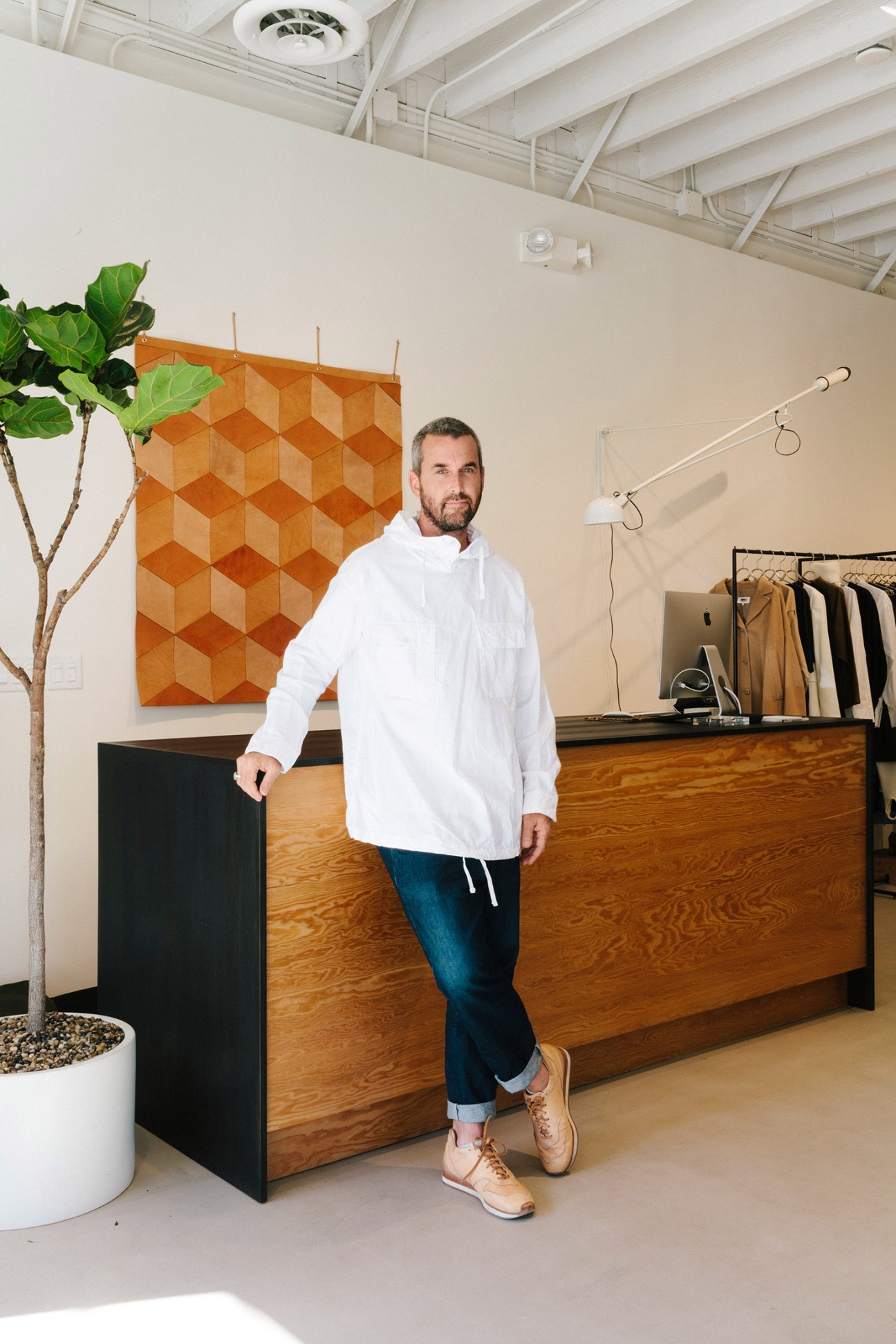 Man in white hoodie and jeans standing in retail space with wooden counter and orange geometric wall art.