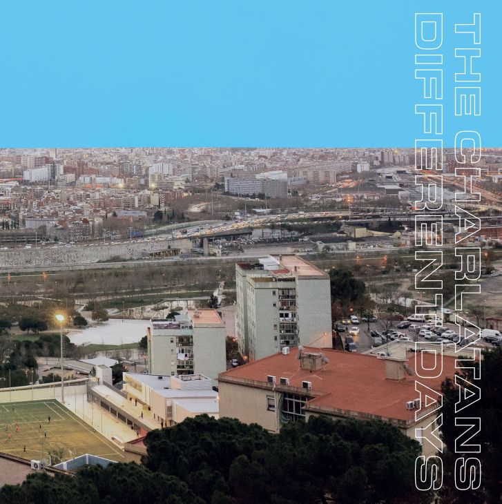 Aerial view of urban residential buildings with red-tiled roofs overlooking a river valley cityscape under blue sky.