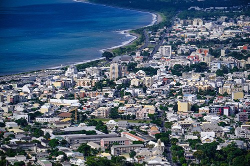 Aerial view of Nouméa, New Caledonia's capital, showing coastal city with buildings and blue ocean.