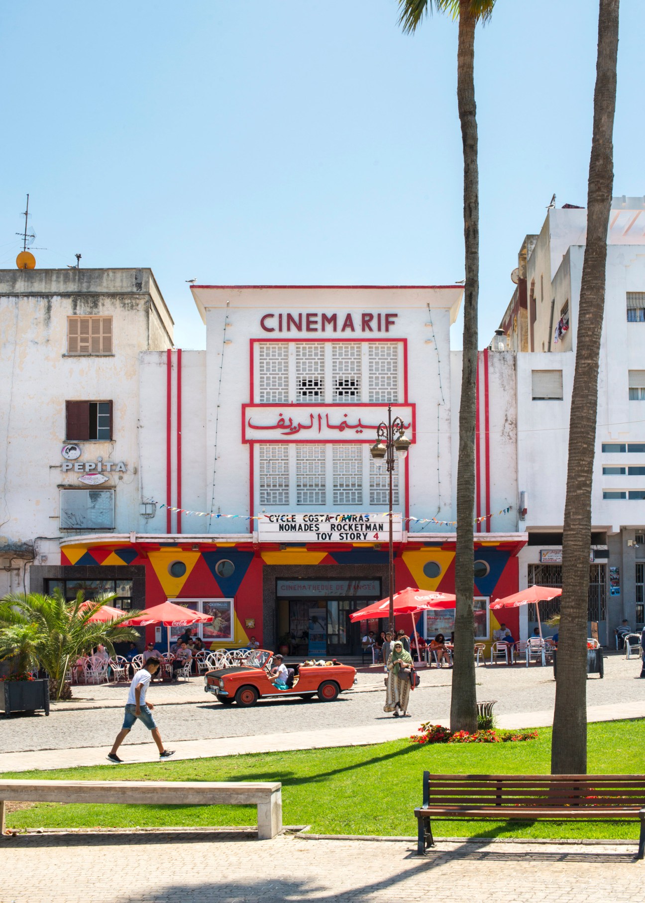 Cinema Rif in Tangier with red and white facade, palm trees, and red umbrellas in the plaza.
