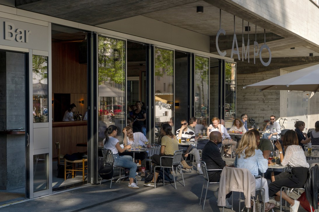 Outdoor terrace of Campo Bar in Zürich with diners seated at tables under a modern canopy.