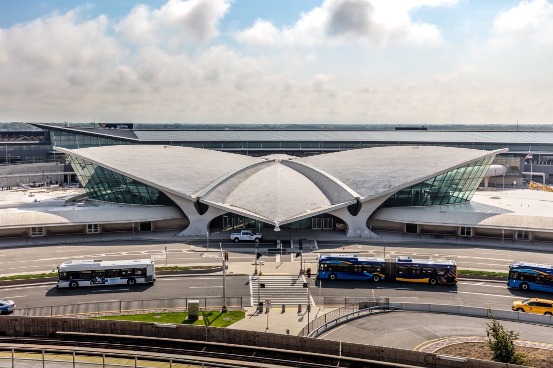 TWA Flight Center terminal building with distinctive white curved architecture and buses on forecourt.