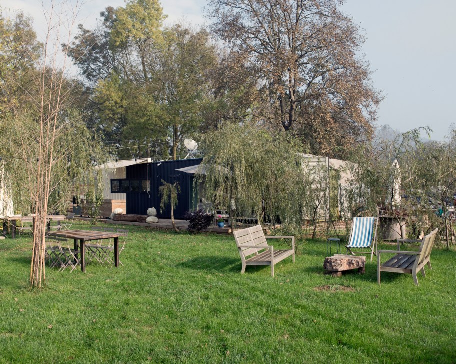 Black cabin structure surrounded by lounge chairs and young trees on green lawn at Komsukoy farm.