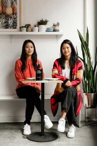 Hannah and Marian Cheng, founders of Mimi Cheng's, seated together holding a bottle of their product.