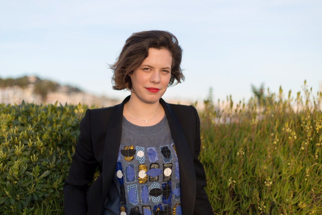 Alice Cabaret, founder of The Street Society, poses outdoors in a black blazer among coastal vegetation.
