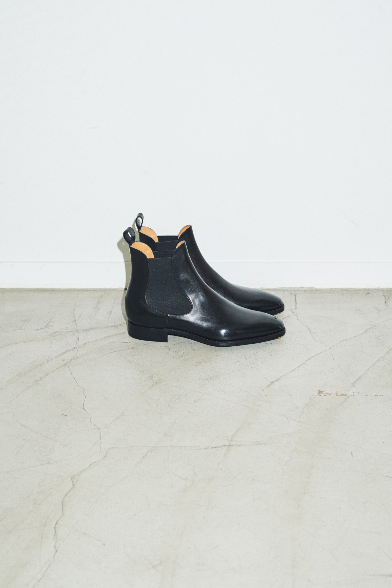Black leather Chelsea boots displayed on white marble surface with yellow shoe trees inside.