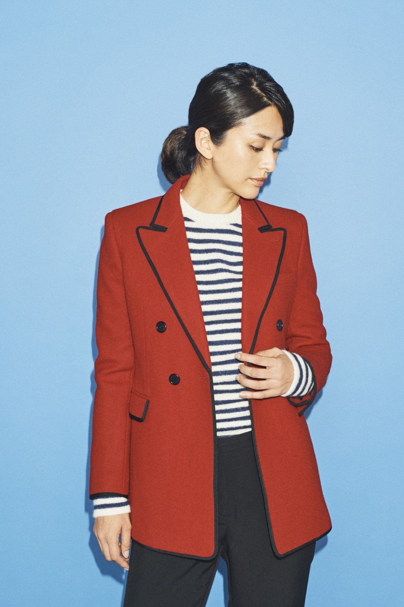 Woman in Saint Laurent jacket and jumper with Emporio Armani trousers against blue background.