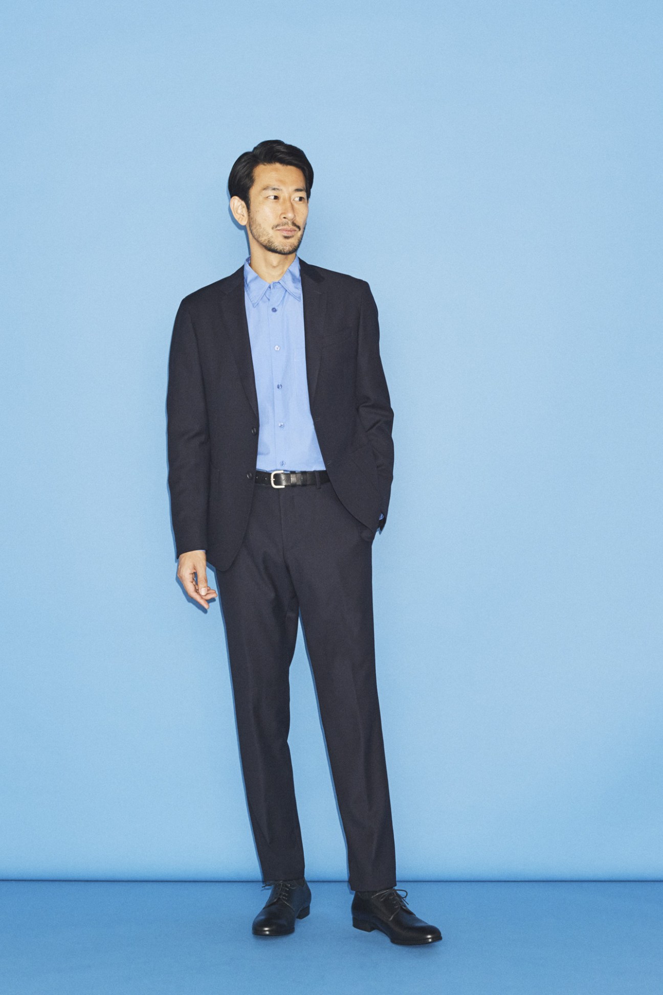 Man in dark suit with light blue shirt standing against blue background