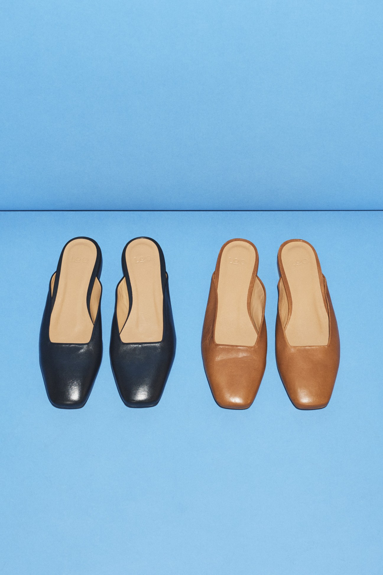 Two pairs of leather mules in black and tan displayed on blue background.