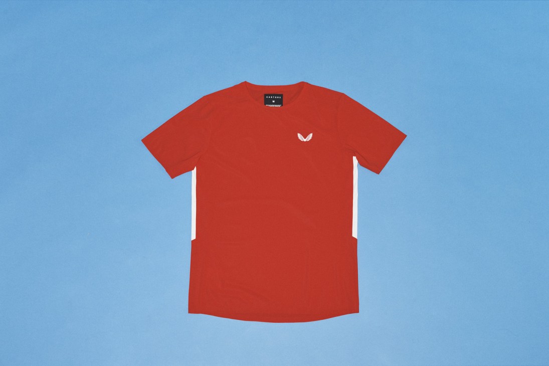 Red t-shirt with small white chevron logo on chest against blue background